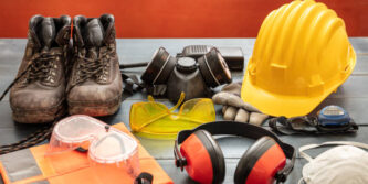 Work safety protection equipment. Industrial protective gear on wooden table, red color background. Construction site health and safety concept